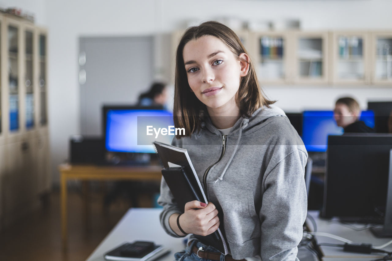 Portrait of confident high school female student with books in classroom