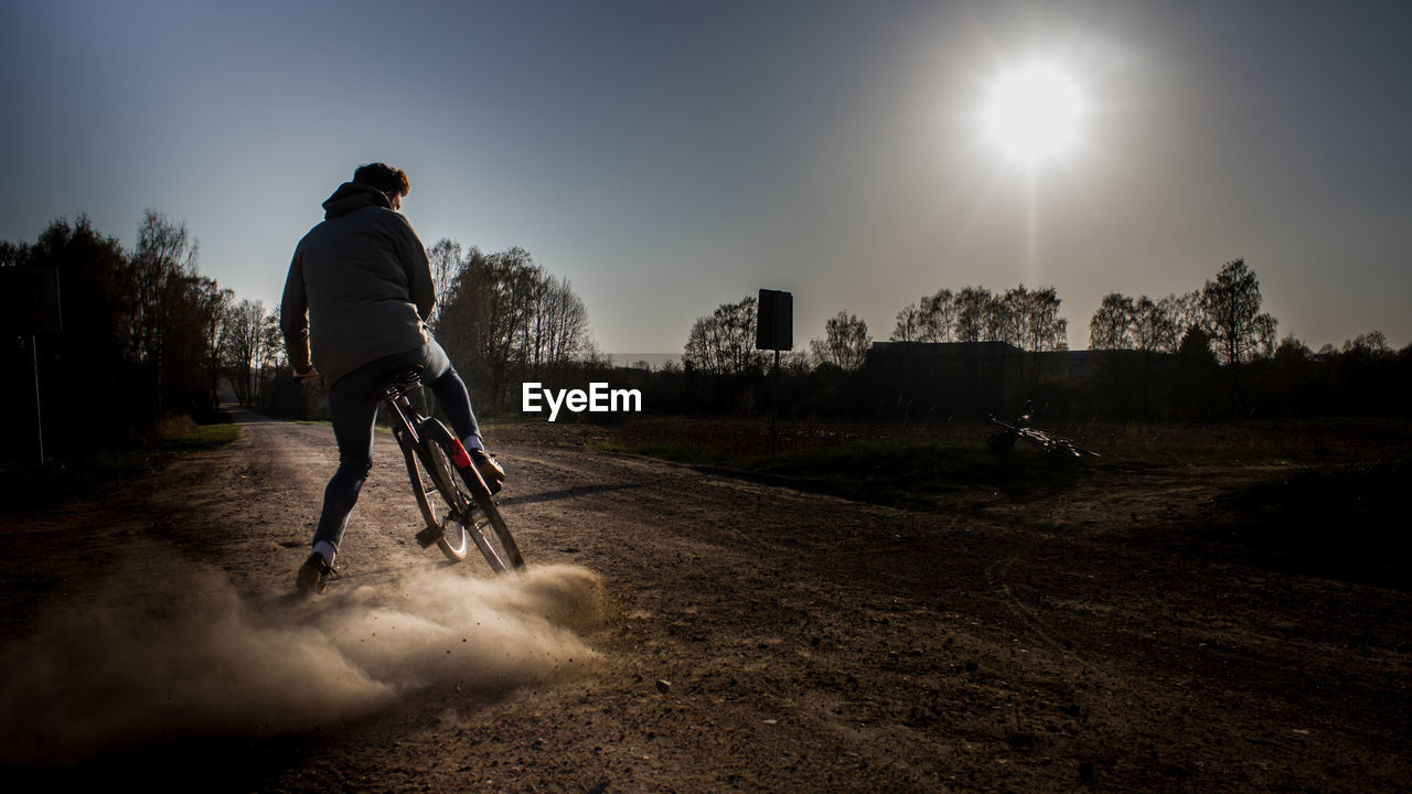 Rear view of man riding bicycle on dirt road