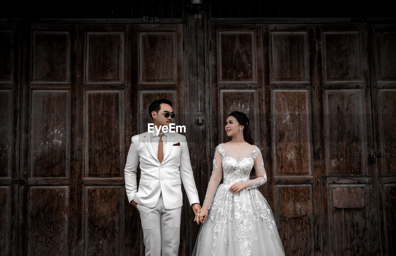 Newlywed couple holding hands while standing against wall