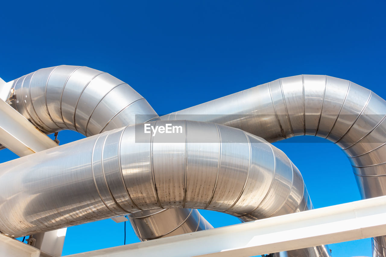 Low angle view of silver pipeline against clear blue sky