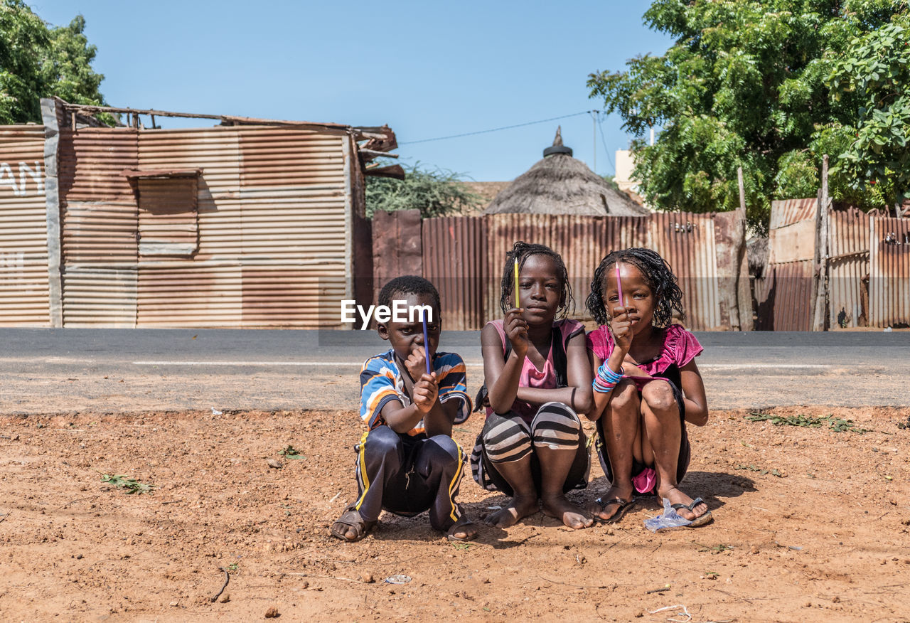 FULL LENGTH PORTRAIT OF PEOPLE SITTING AGAINST BUILDING