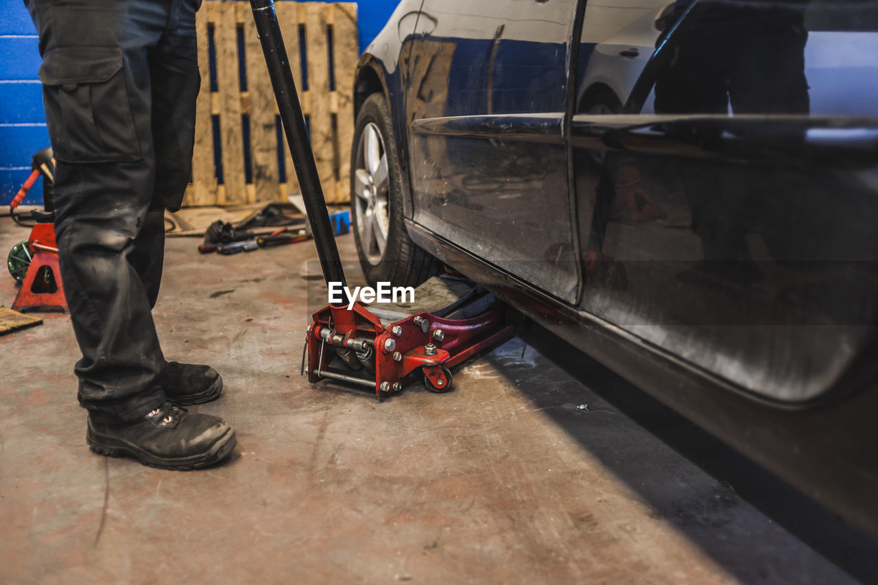 Unrecognizable technician lifting modern vehicle with hydraulic jack during work in professional garage