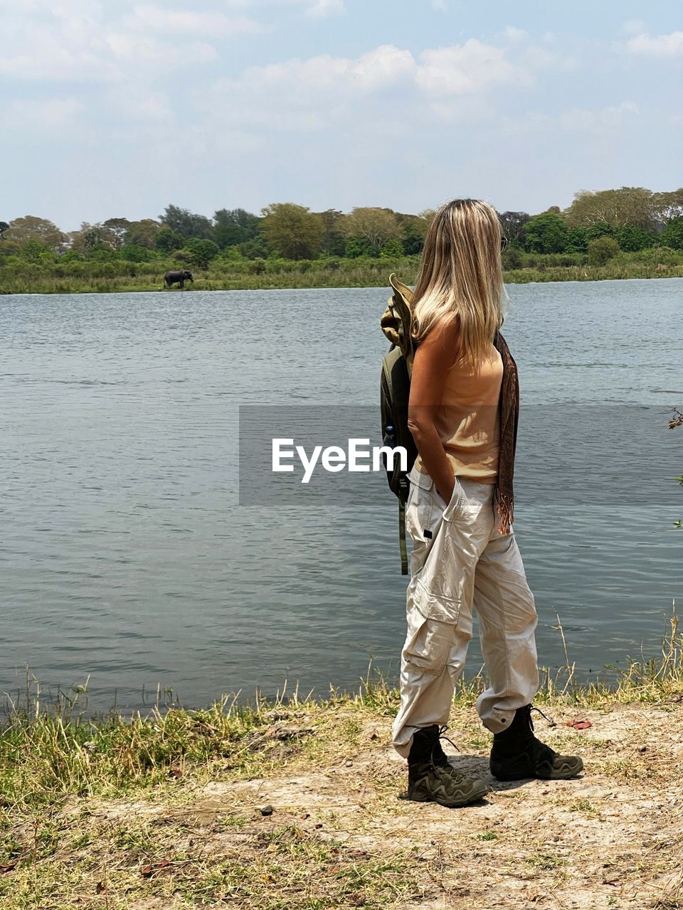 water, nature, lake, full length, one person, rear view, adult, blond hair, leisure activity, sky, women, day, casual clothing, long hair, standing, lifestyles, shore, beauty in nature, plant, hairstyle, trip, vacation, cloud, holiday, outdoors, lakeshore, person, tranquility, beach, female, activity, clothing, environment, scenics - nature, childhood, land, travel, child, fishing, sunlight, grass, non-urban scene, young adult, landscape