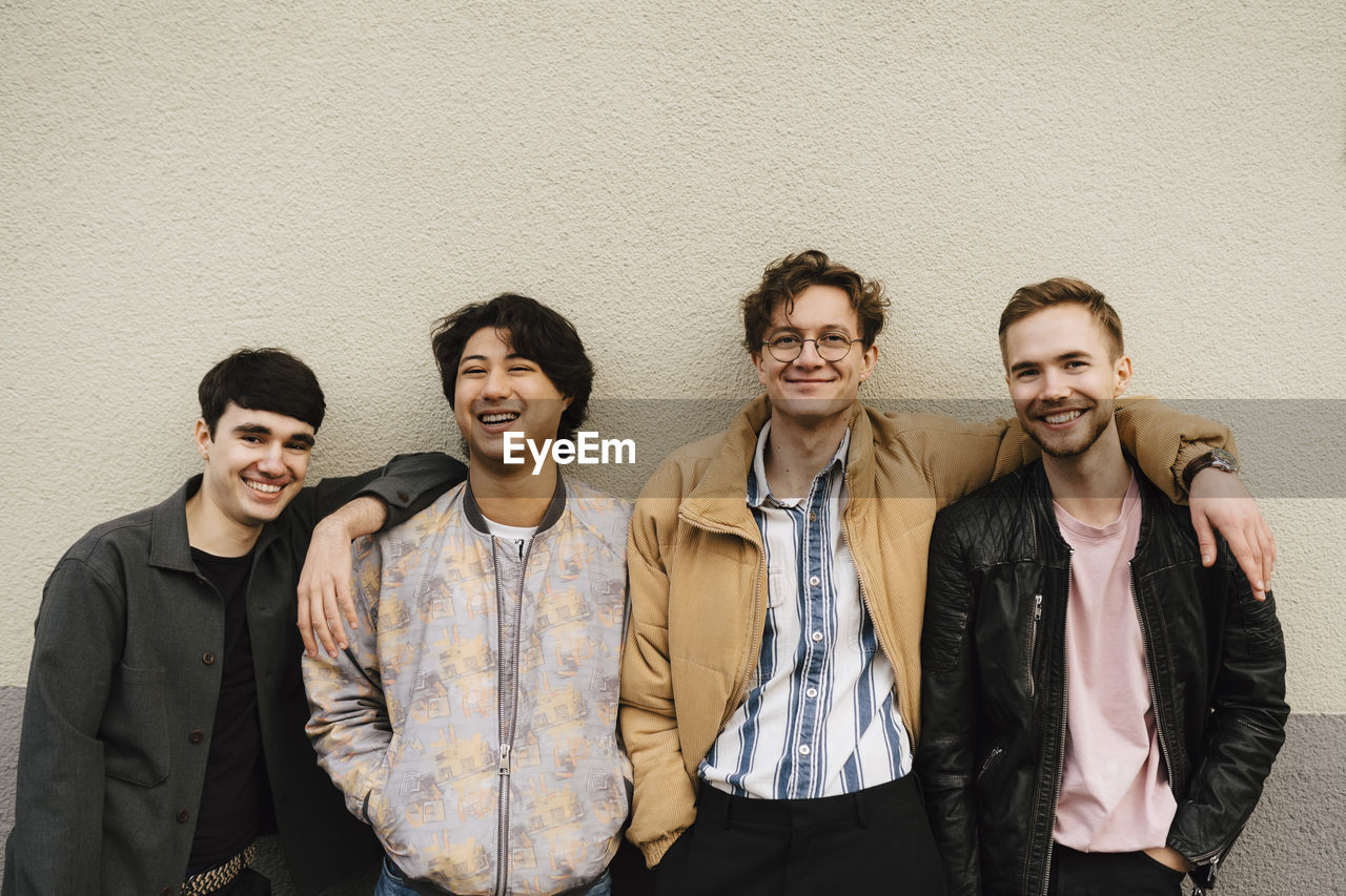 Portrait of happy multi-ethnic young male friends against beige wall