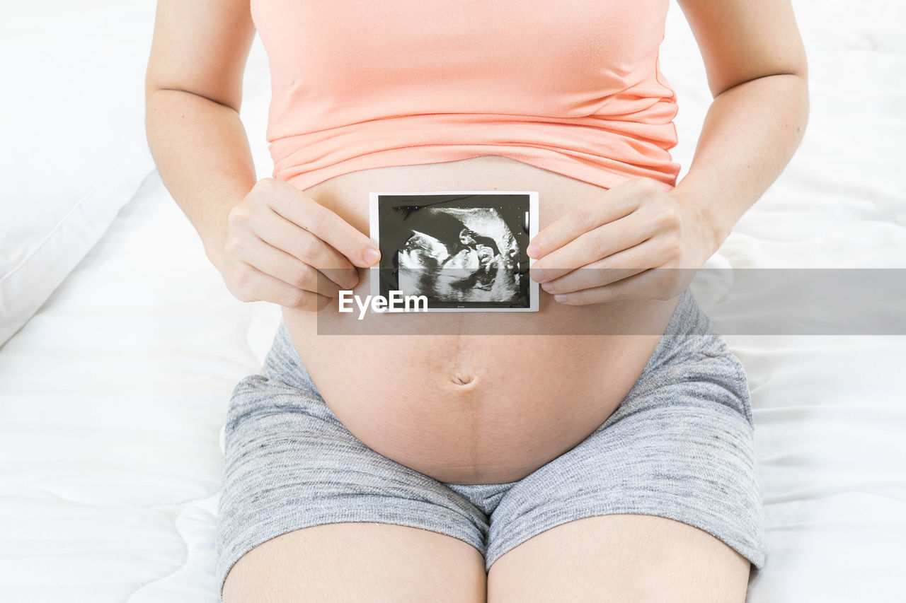 pregnant, adult, one person, midsection, trunk, beginnings, women, anticipation, indoors, clothing, human fertility, parent, undergarment, limb, lifestyles, female, front view, young adult, hope, life events, healthcare and medicine, human leg, person, hands on stomach, sitting, prenatal care, panties, domestic room