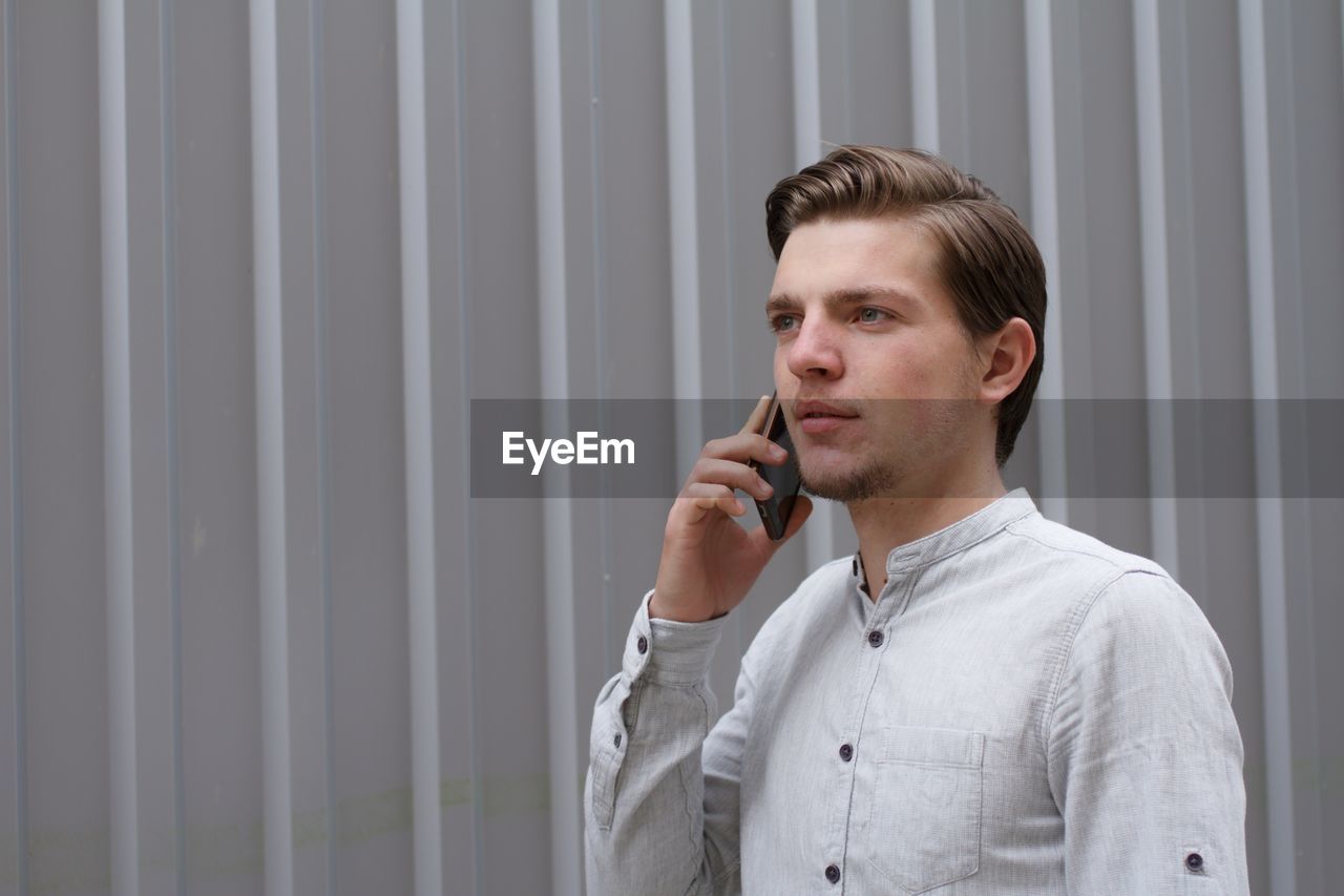 Young man standing against wall talking on mobile phone