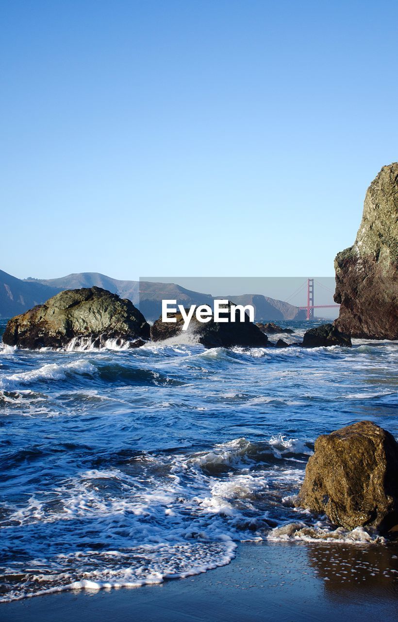 Rocks on beach with suspension bridge in background