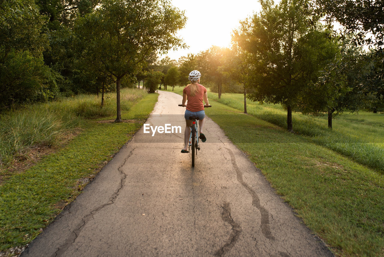 Rear view of young woman riding bicycle on road while wearing a helmet