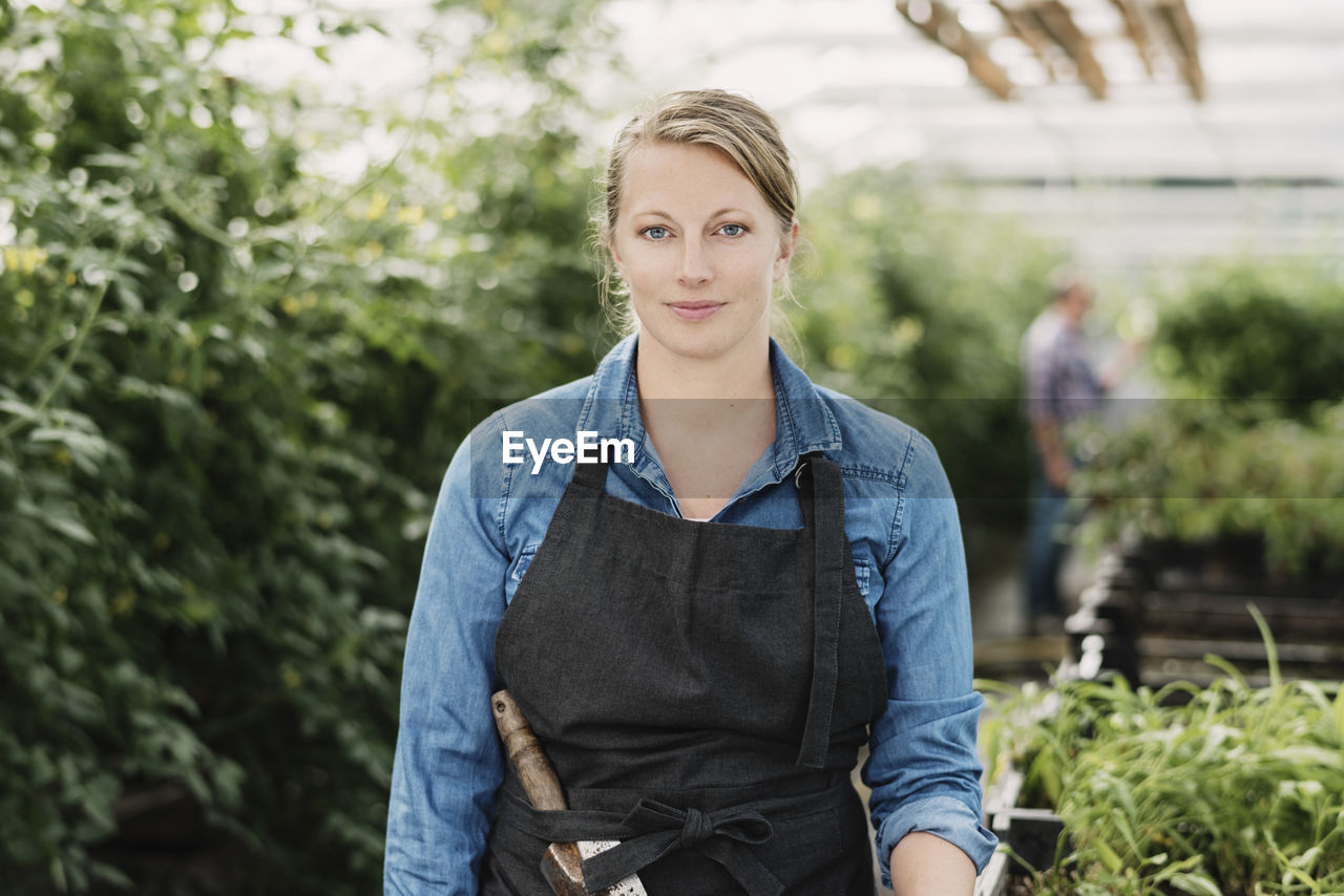 Portrait of confident female gardener standing in greenhouse
