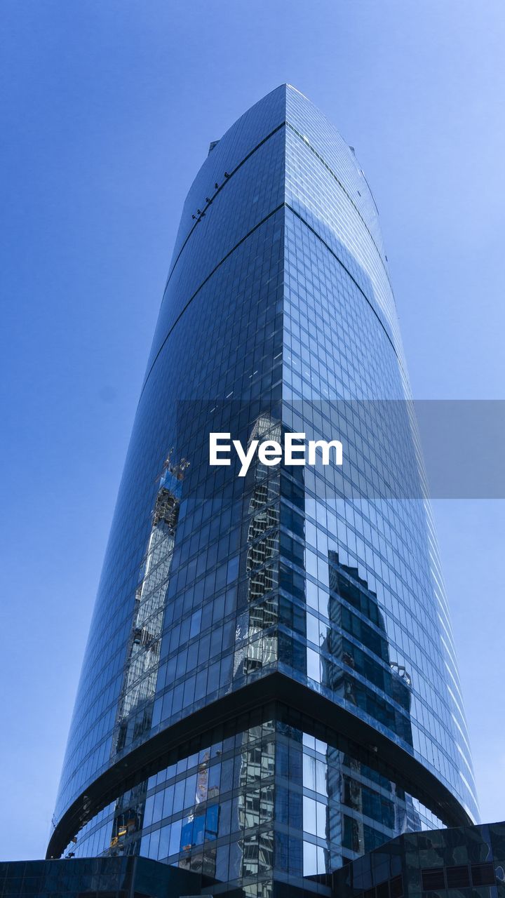 LOW ANGLE VIEW OF MODERN GLASS BUILDING AGAINST BLUE SKY