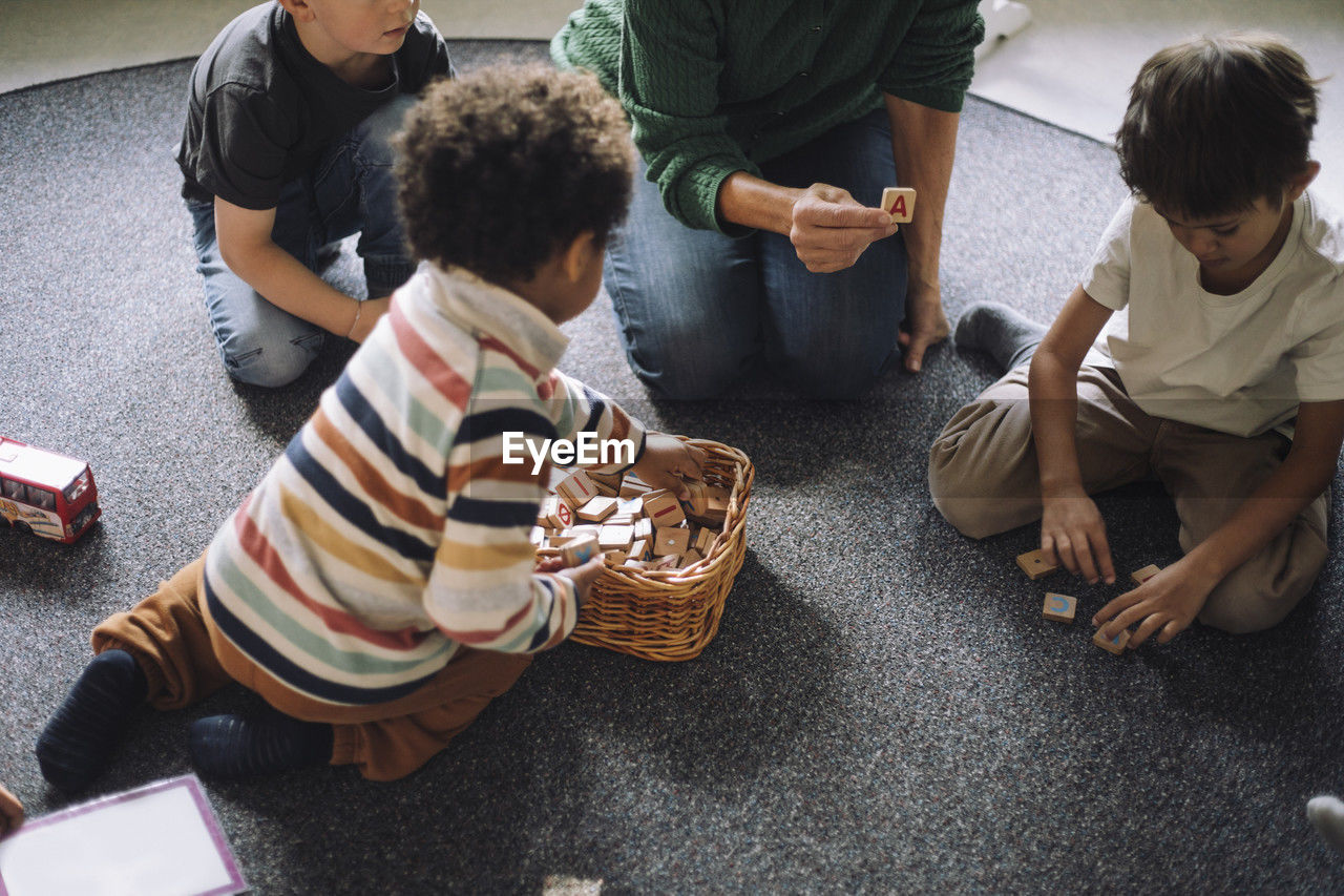 High angle view of schoolboys playing puzzle game with female teacher in classroom at kindergarten