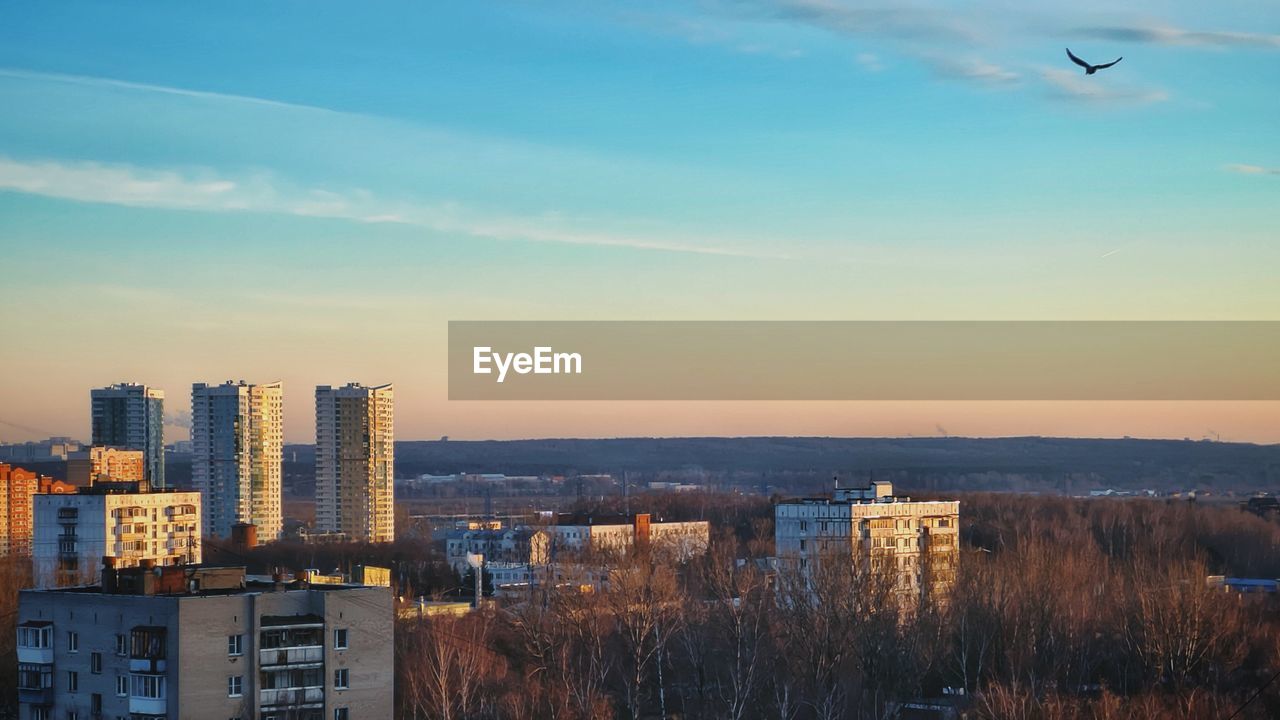 High angle view of buildings against sky during sunset. bird starts fly above city.