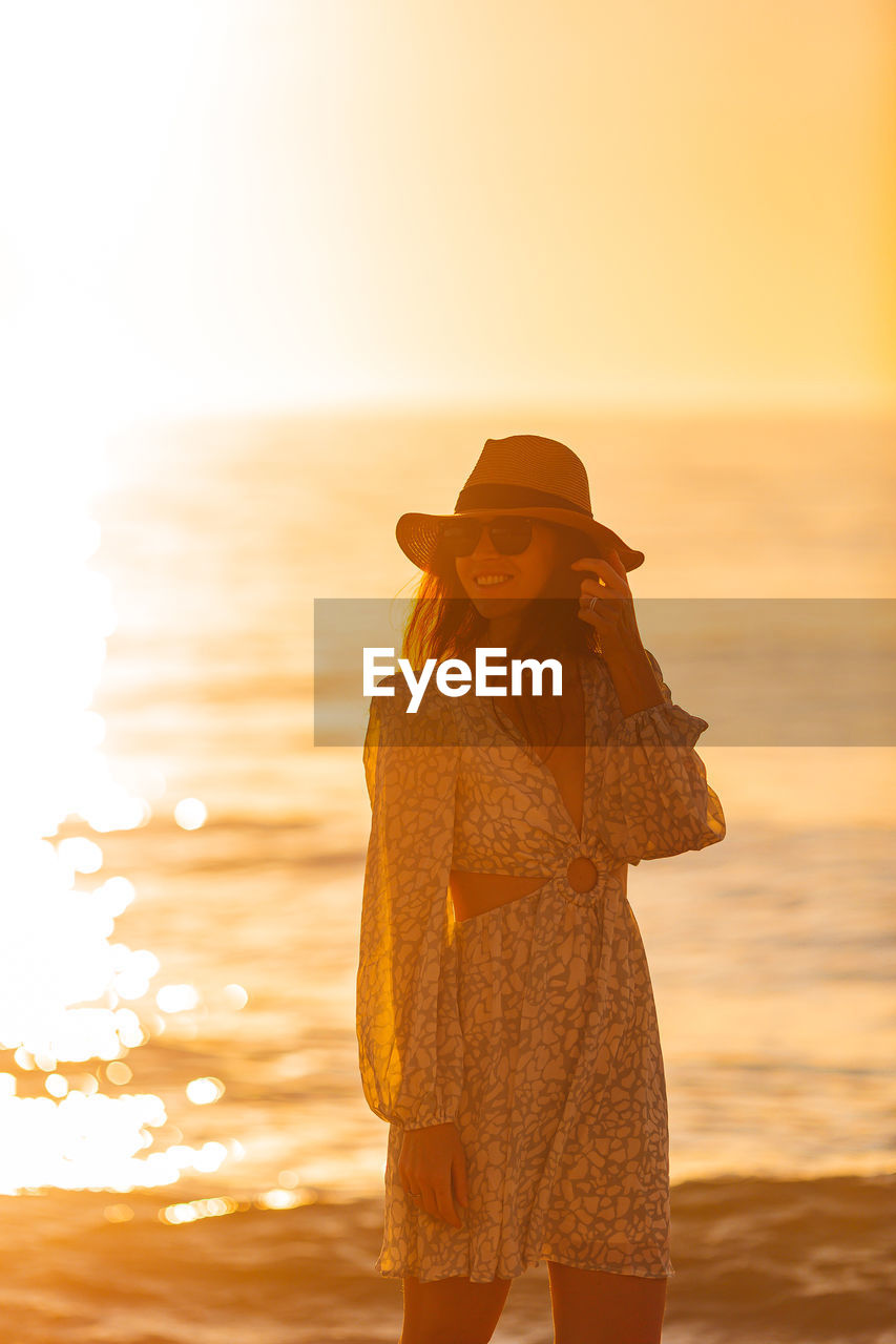 rear view of woman standing at beach against sky during sunset