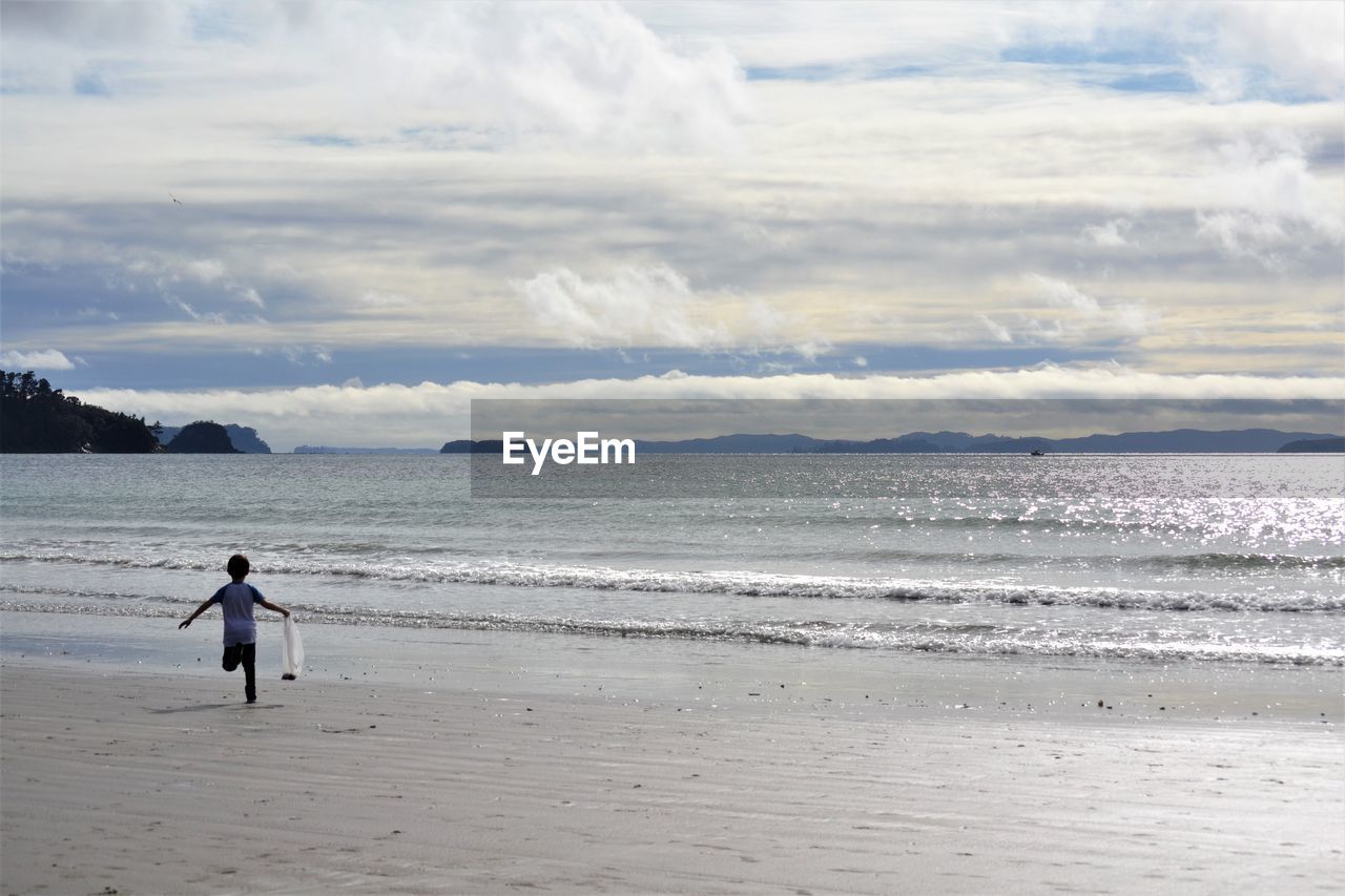 WOMAN STANDING ON BEACH AGAINST SKY