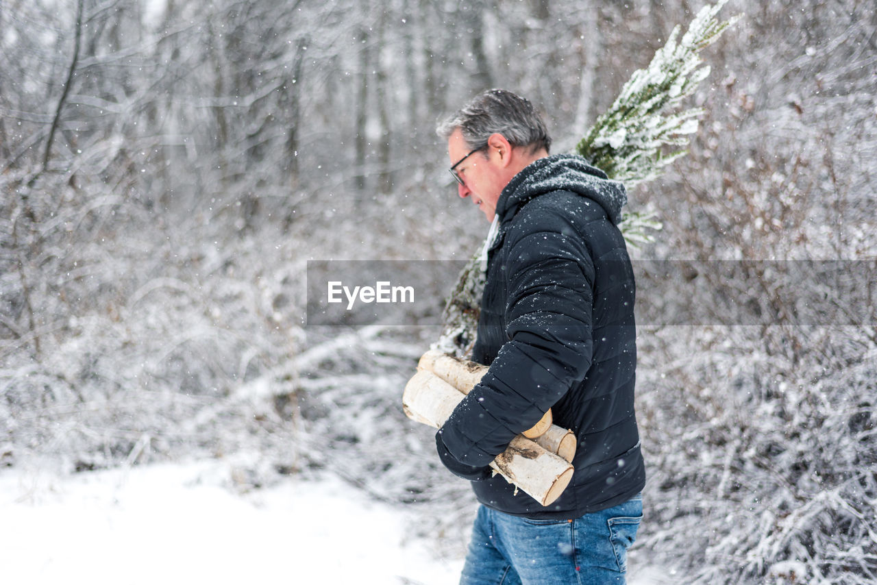 Side view of man carrying firewood during winter