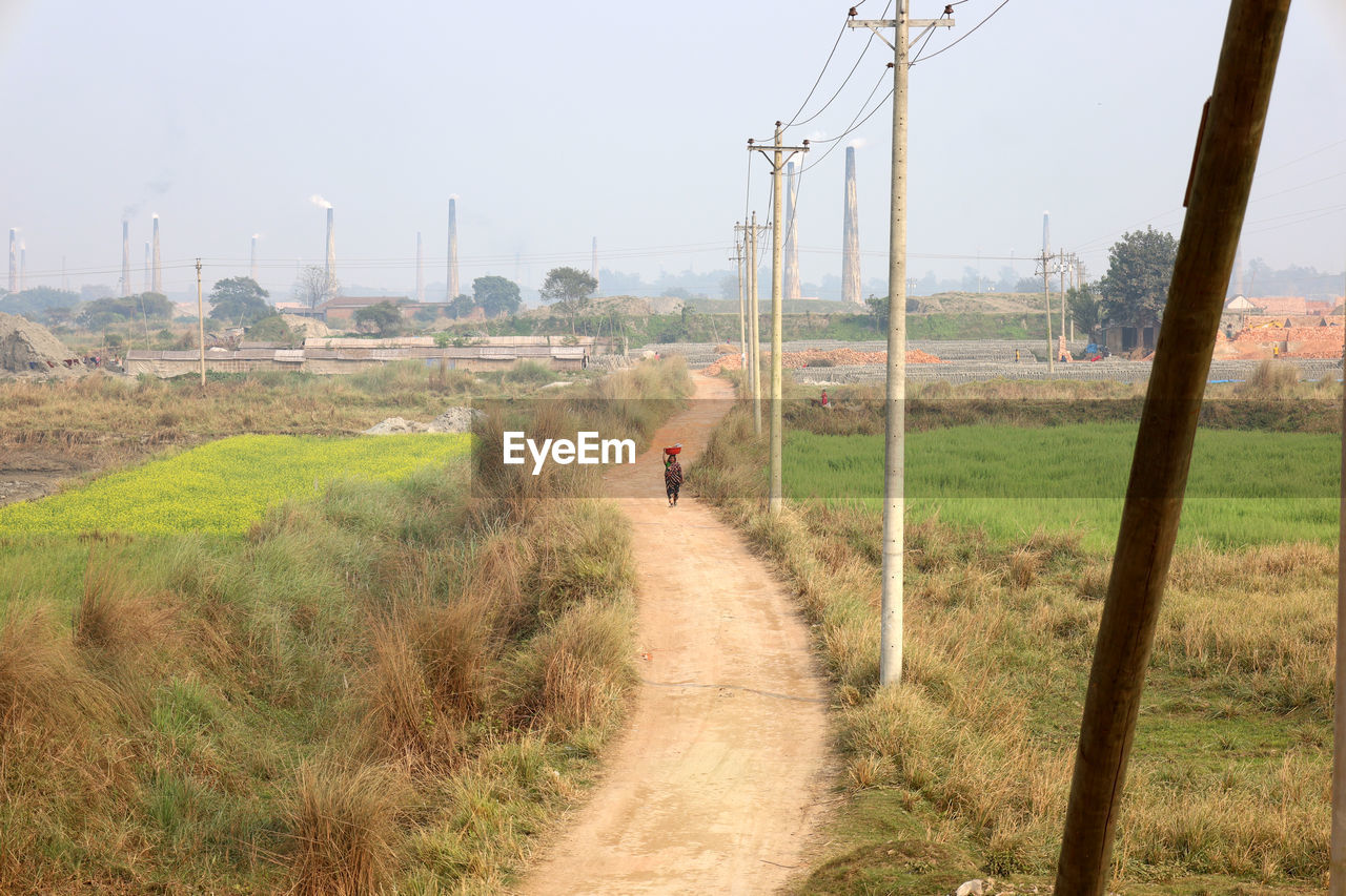 landscape, environment, rural area, nature, sky, plant, land, road, transportation, electricity, rural scene, transport, hill, grass, field, electricity pylon, day, architecture, dirt, outdoors, agriculture, technology, scenics - nature, travel, soil, dirt road, power generation, cable, built structure, track, city, environmental conservation, tree, waterway, social issues, prairie, beauty in nature, footpath, power line, travel destinations, natural environment