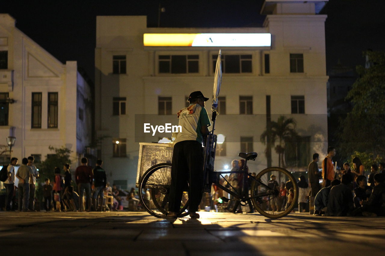 Man with bicycle on street in city at night