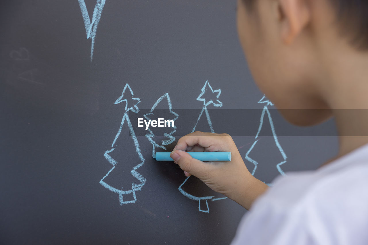 Close-up of boy drawing christmas tree on blackboard