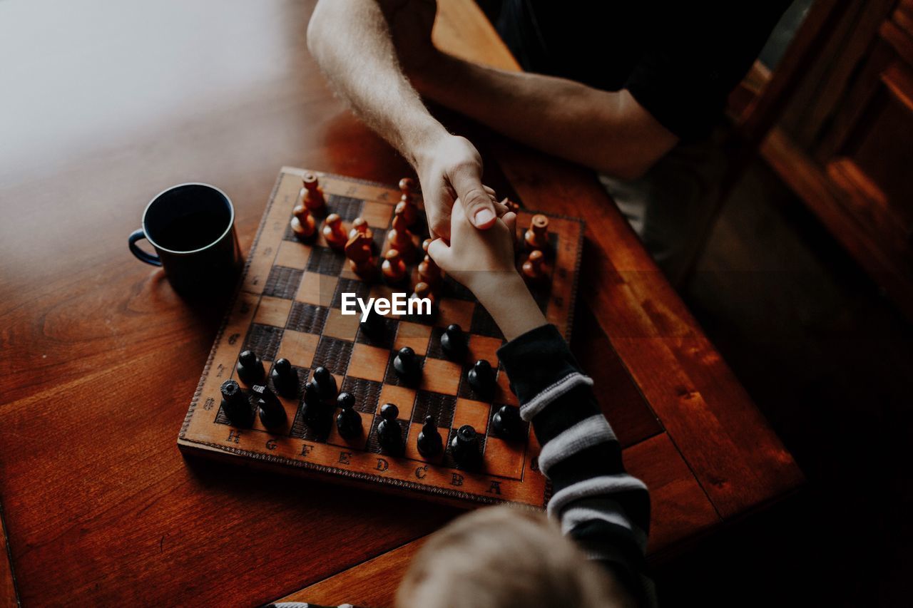 High angle view of people holding hands over chess board on table