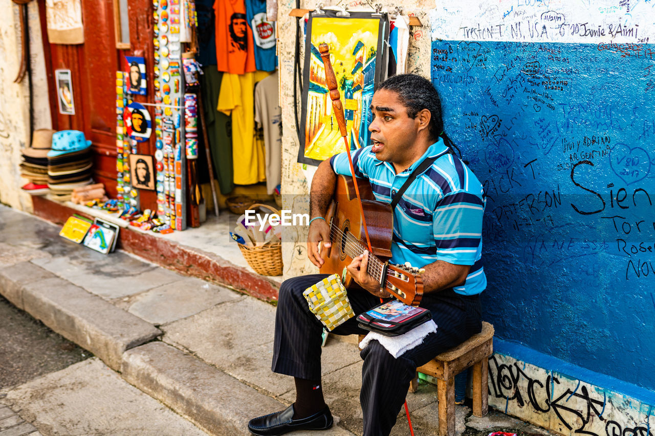 FULL LENGTH OF BOY SITTING ON MULTI COLORED GRAFFITI ON WALL