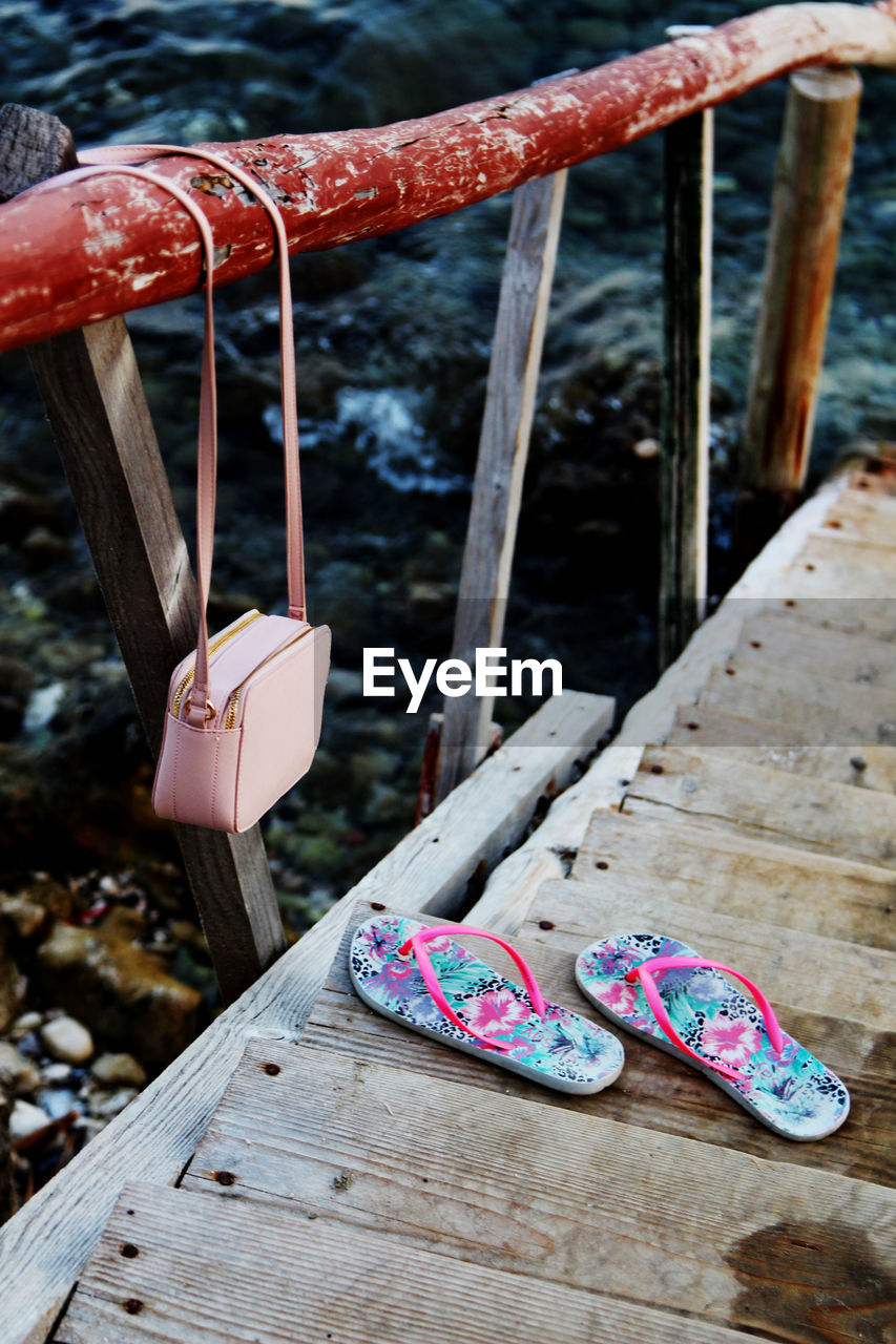 High angle view of flip-flops on wooden bridge by bag hanging on railing