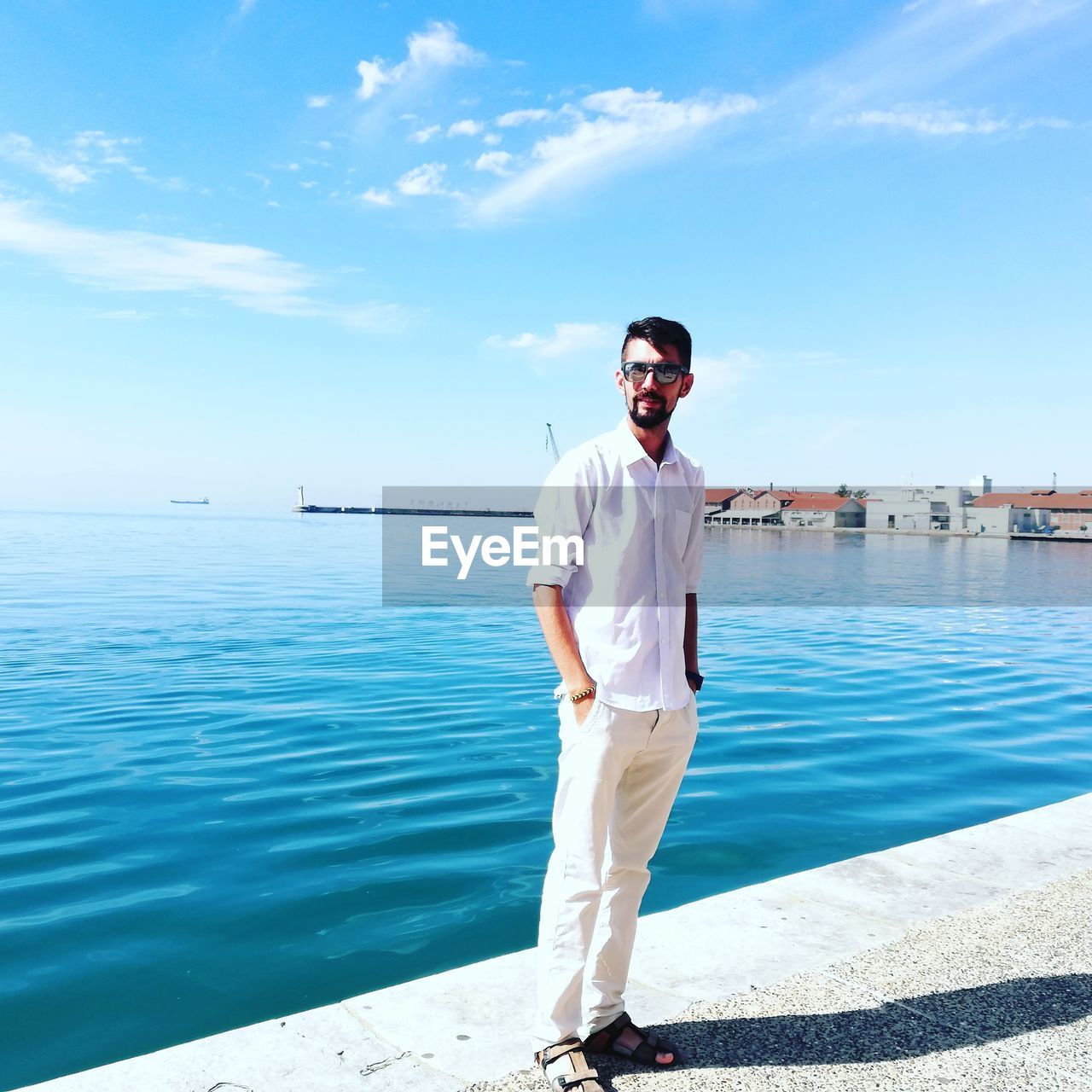 Portrait of man wearing sunglasses while standing on promenade against blue sky