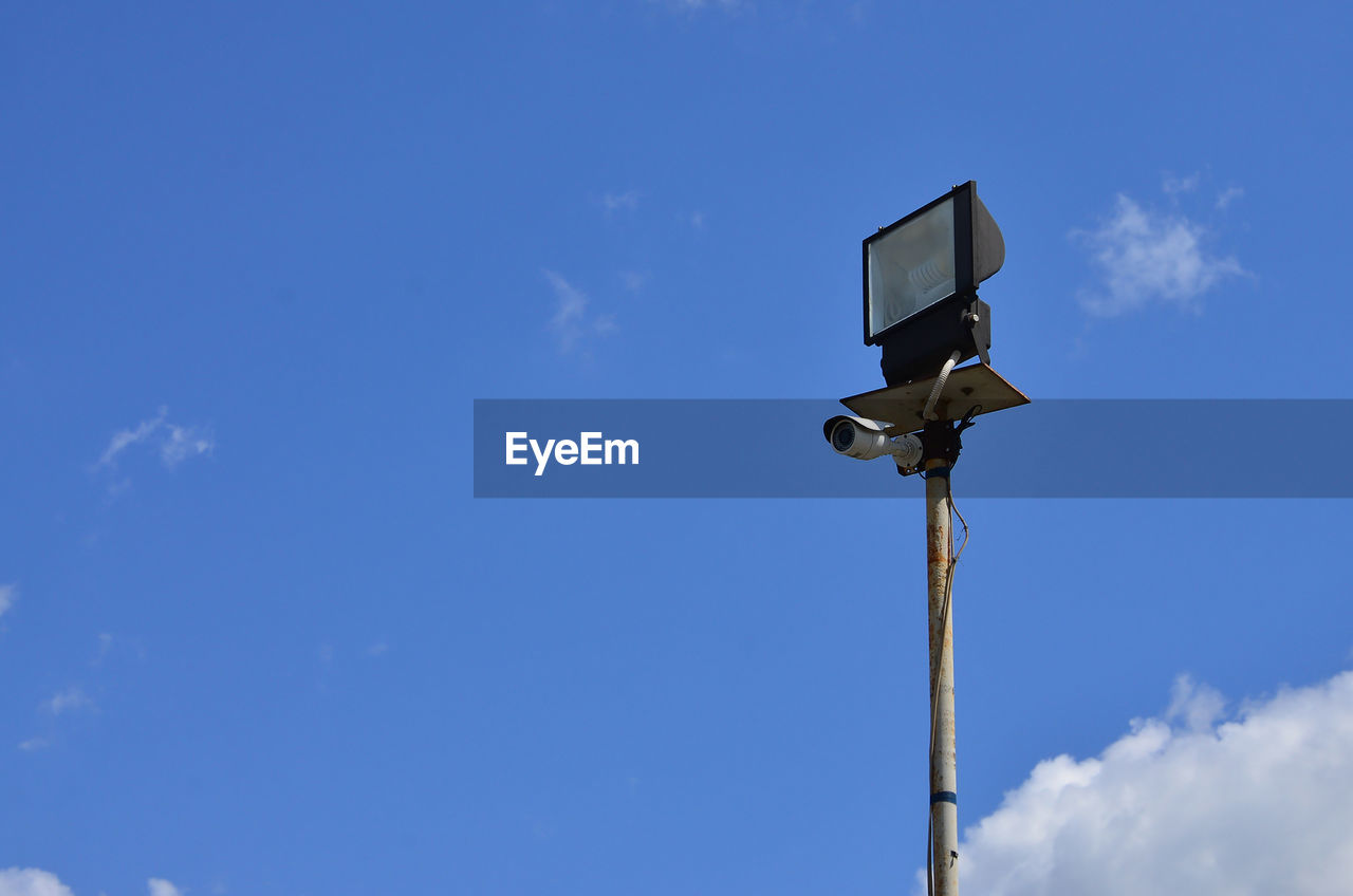 Low angle view of security camera on floodlight against blue sky
