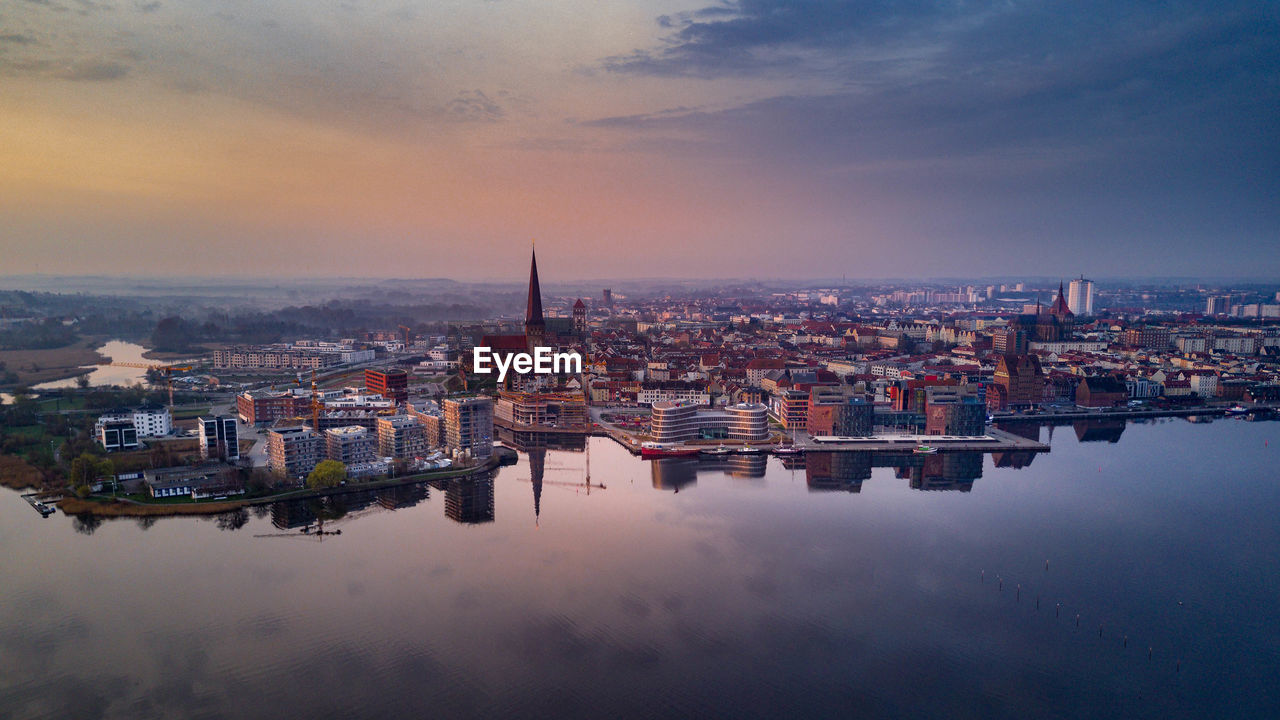 Cityscape by river against sky during sunset