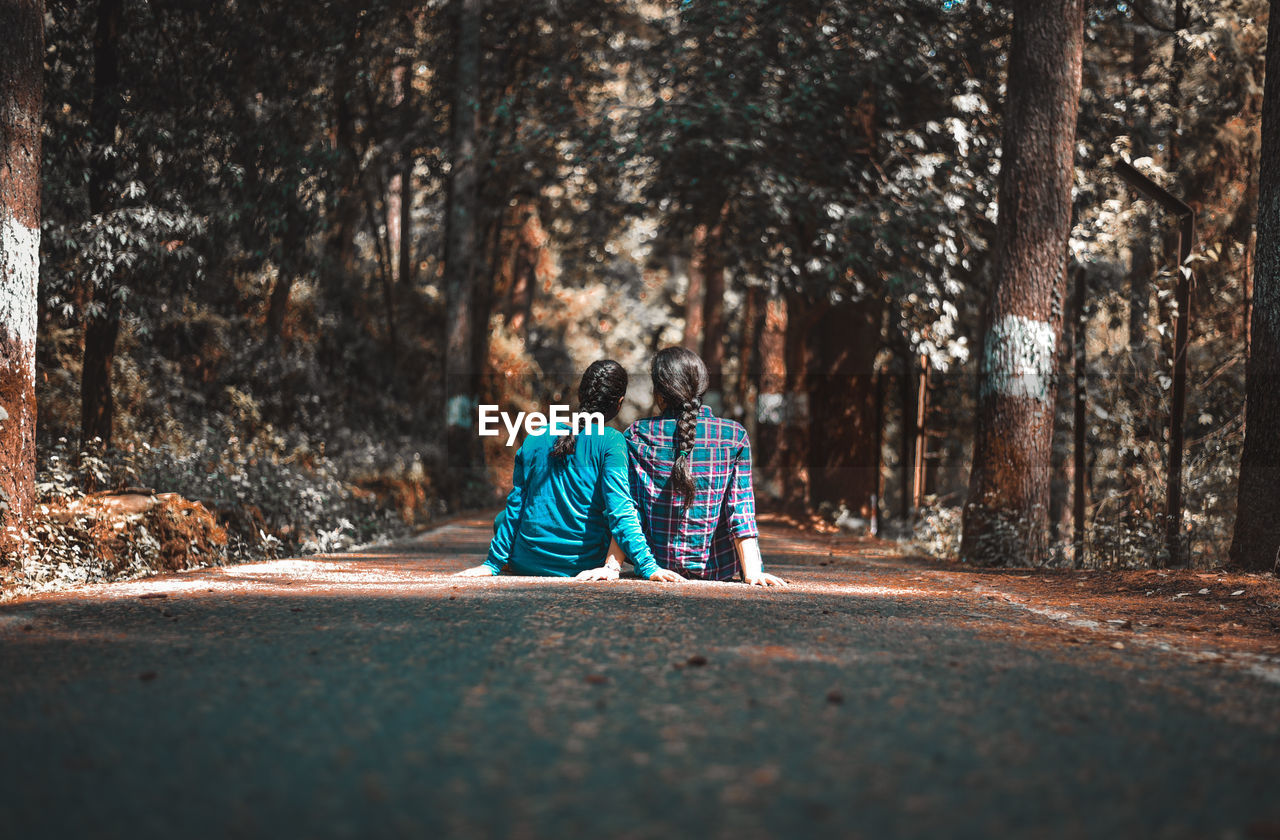 REAR VIEW OF MEN SITTING ON ROAD AMIDST TREES