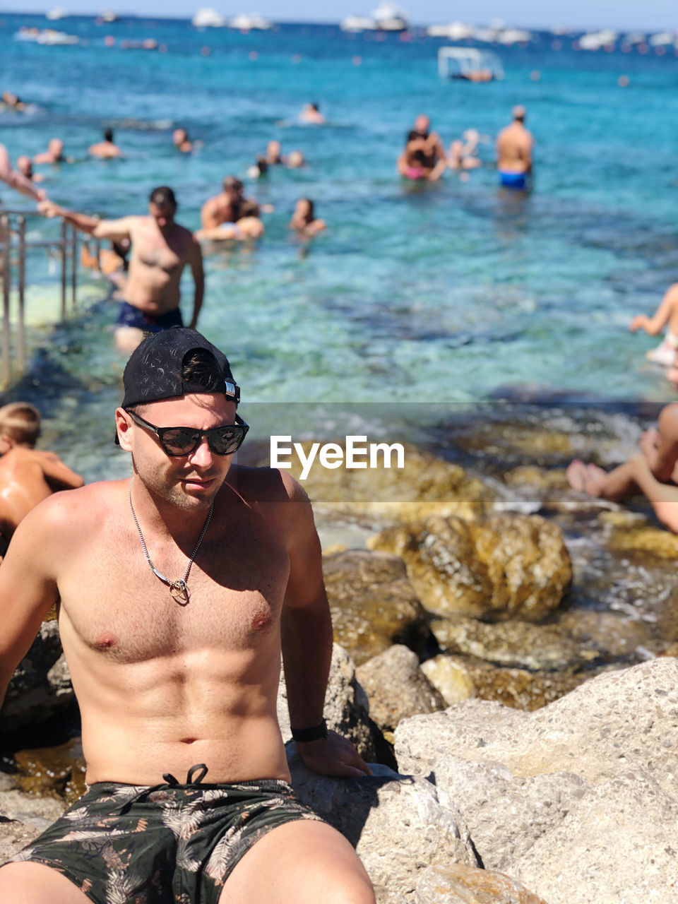 Shirtless man on rock at sea shore