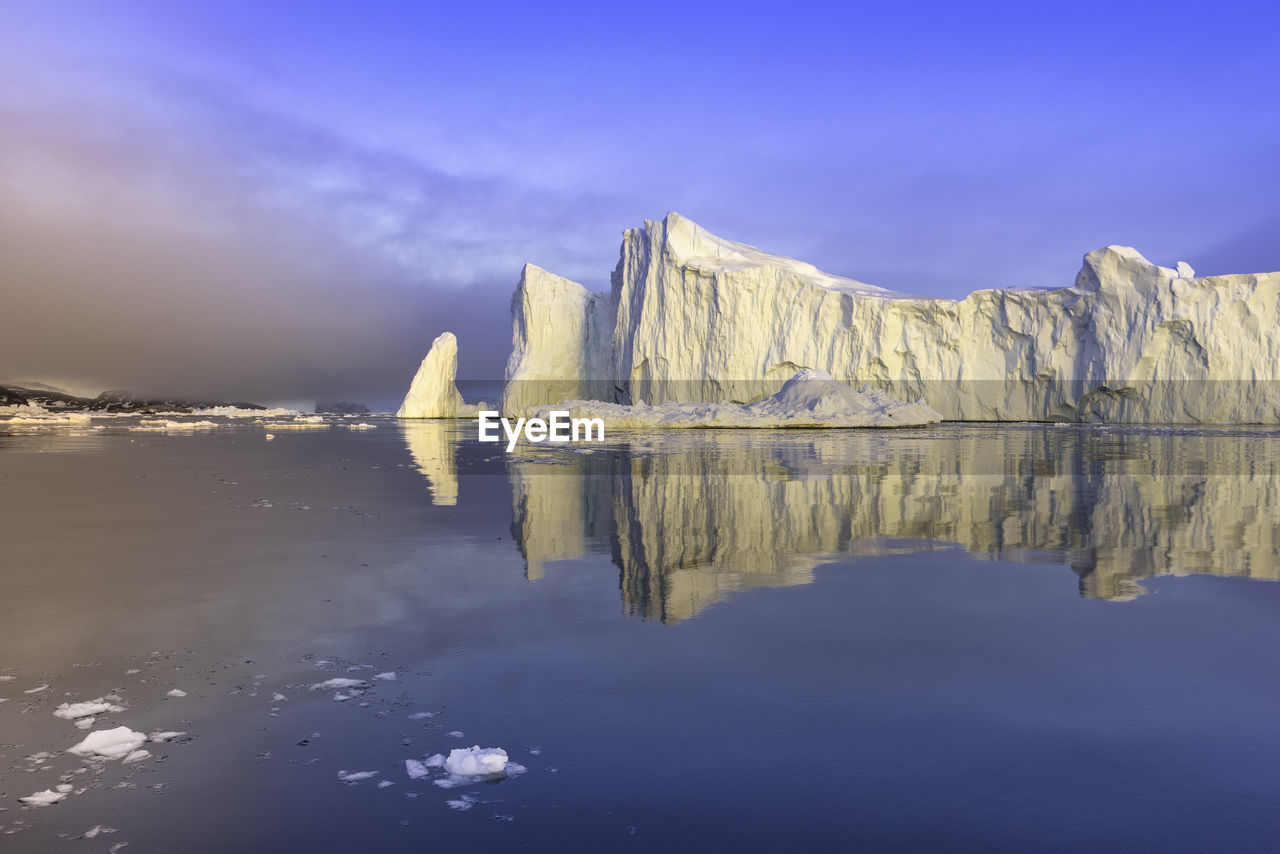 Reflection of glacier on calm sea against sky