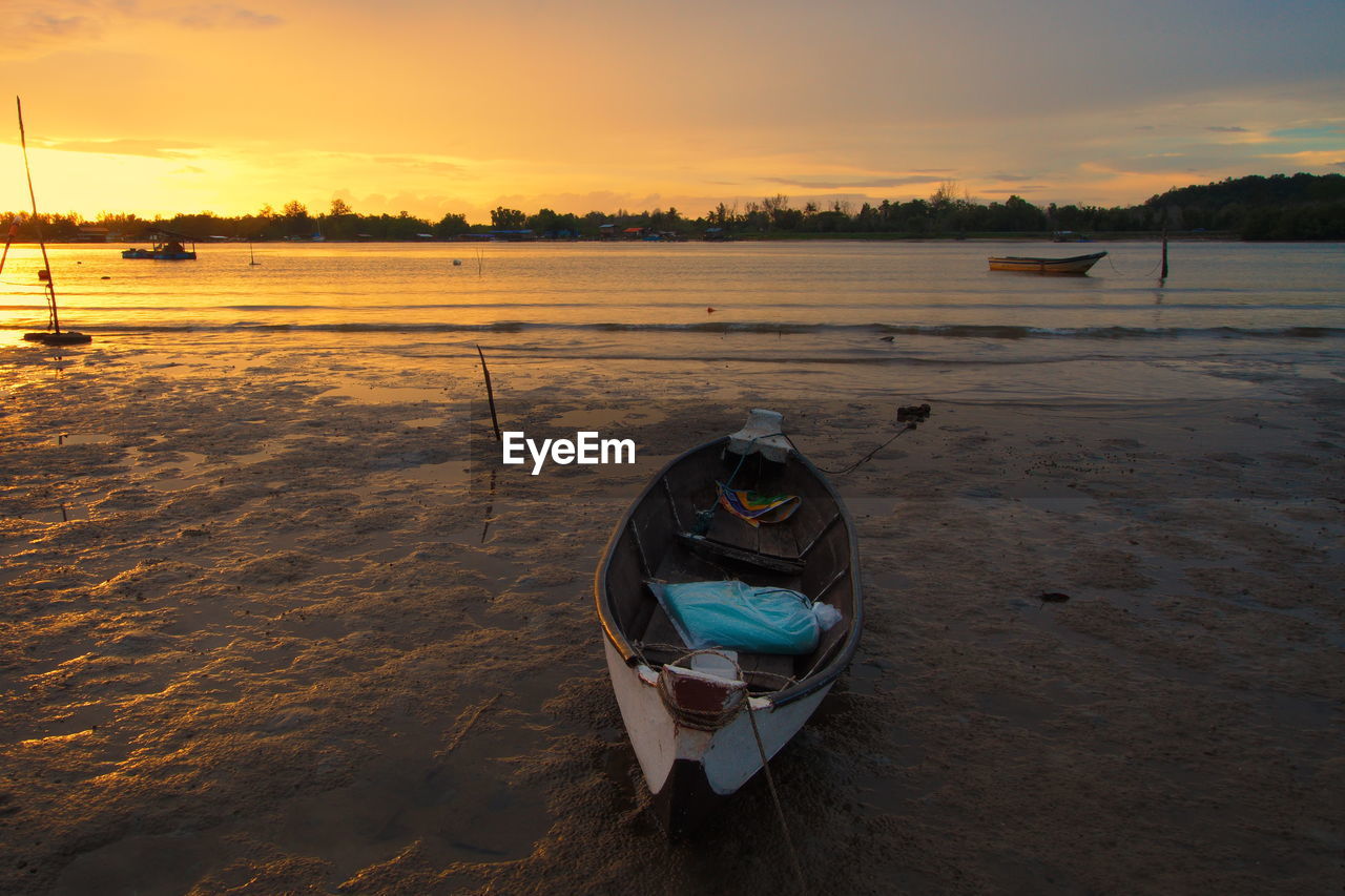 Boat moored on beach against sky during sunset