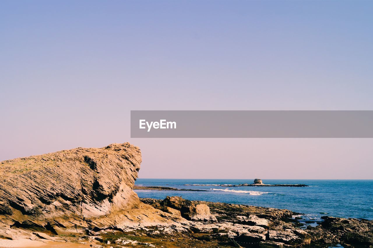 Scenic view of sea and rocks against clear sky