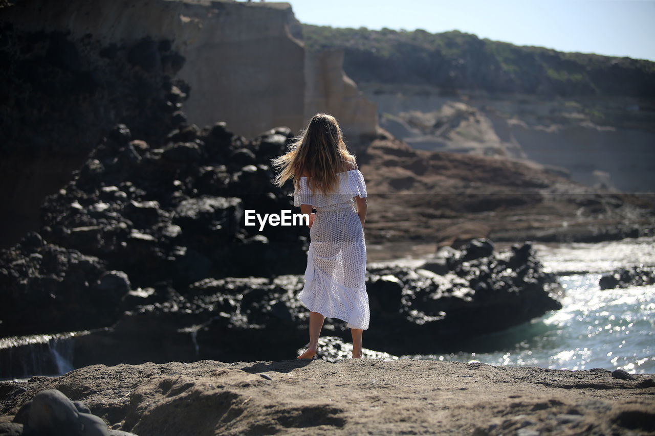 REAR VIEW OF WOMAN STANDING ON ROCK