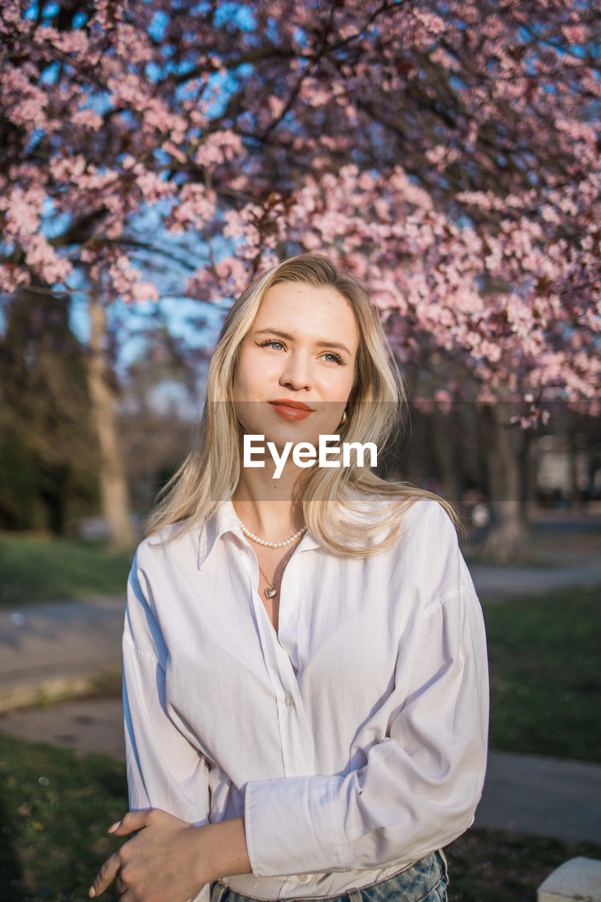 portrait of smiling young woman standing against trees