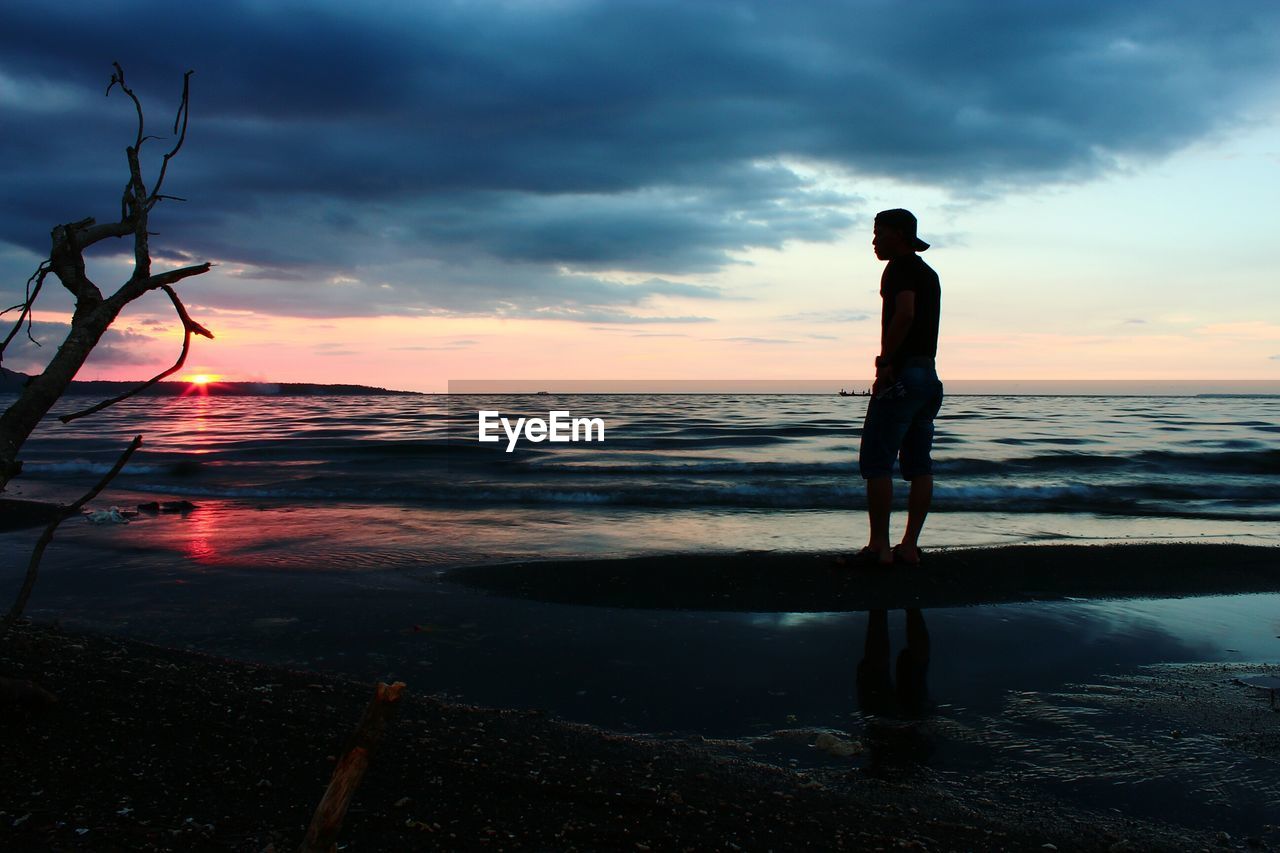 Silhouette man standing on beach against sky during sunset