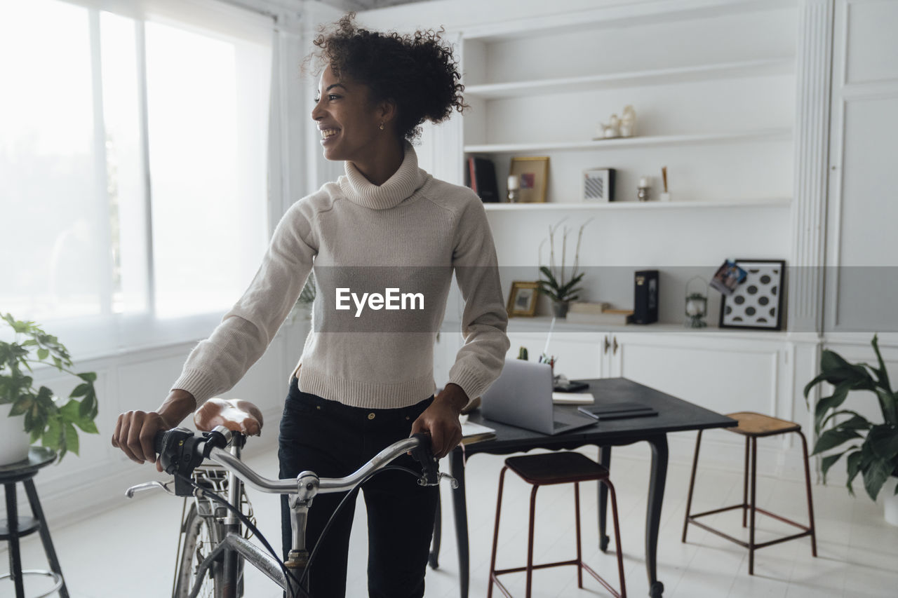 Mid adult woman leaving her home office, pushing bicycle