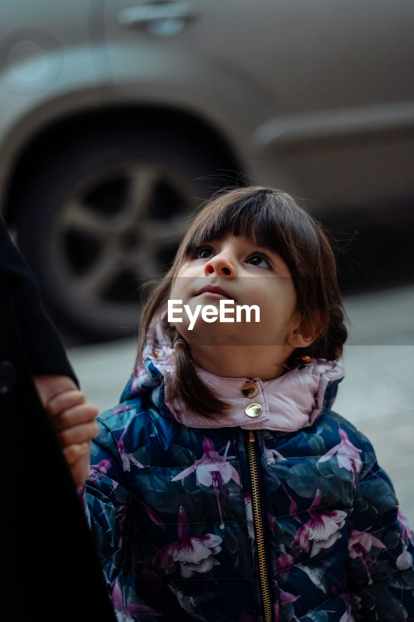 A little girl holds her mother's hand and looks at her with her head thrown back