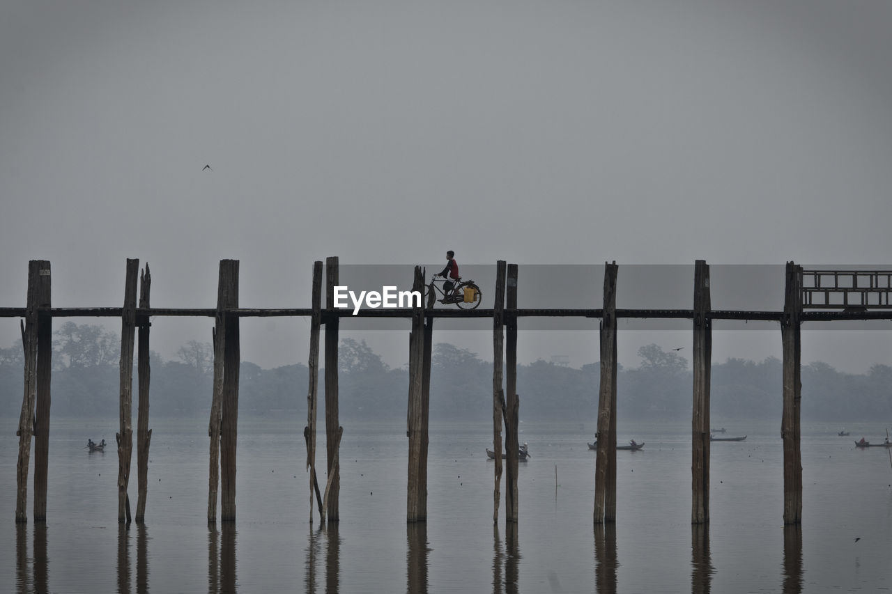 Man riding bicycle on bridge over lake