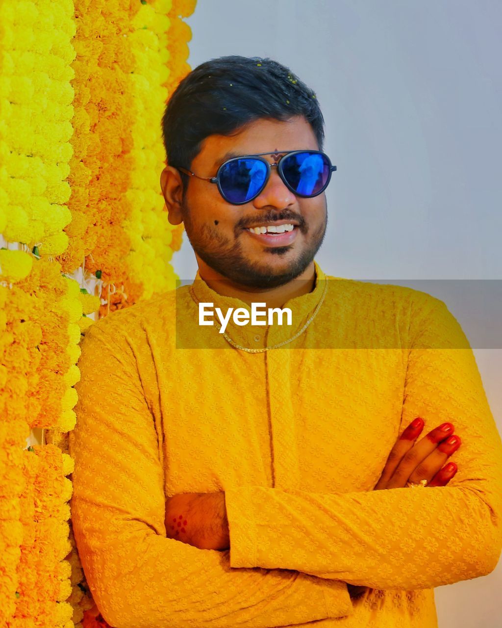 Portrait of young man wearing sunglasses standing against flower wall decoration