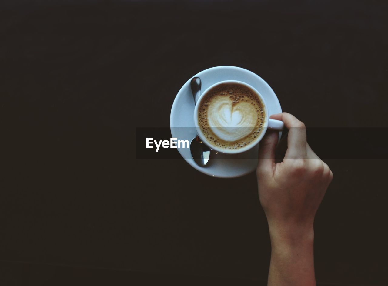 Cropped hand holding coffee with saucer and spoon. dark copyspace. espresso in a cup. 