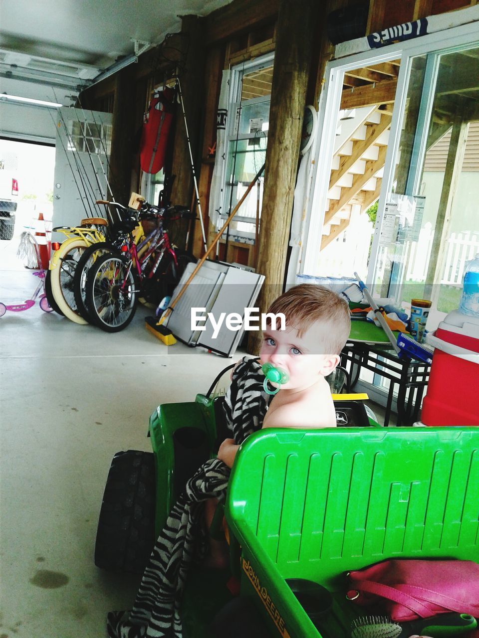 Portrait of boy with pacifier in mouth sitting on toy car