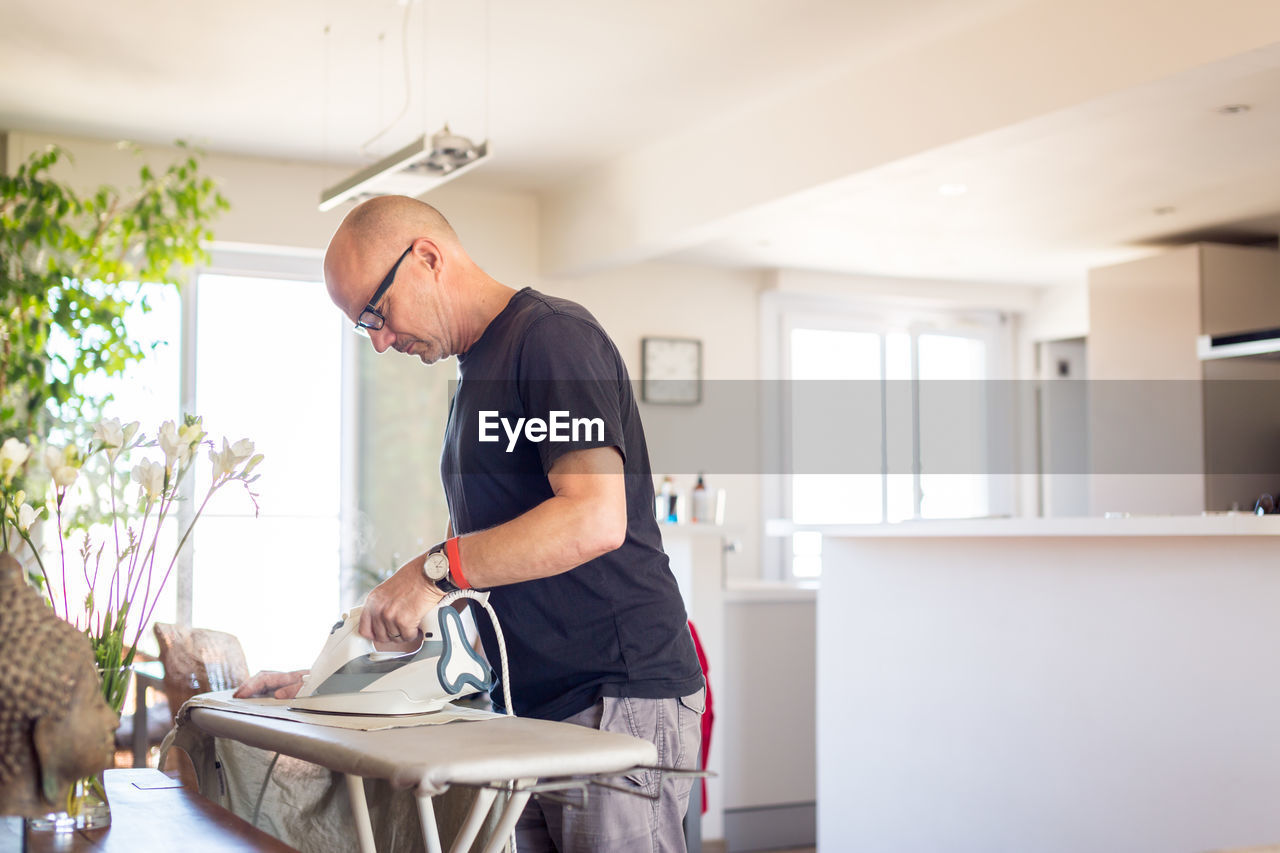 Side view of man ironing clothes on board at home