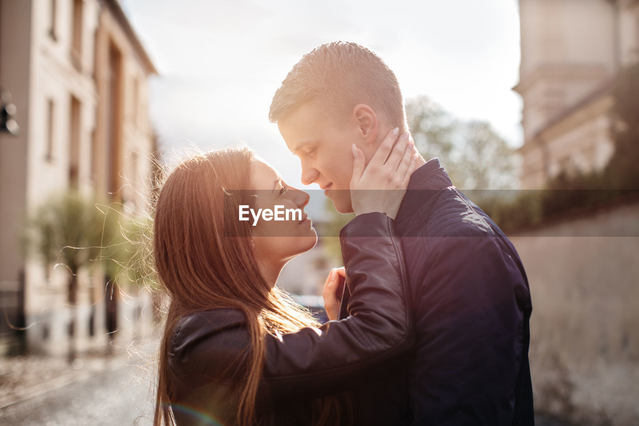 Couple looking at each other while standing amidst buildings against sky