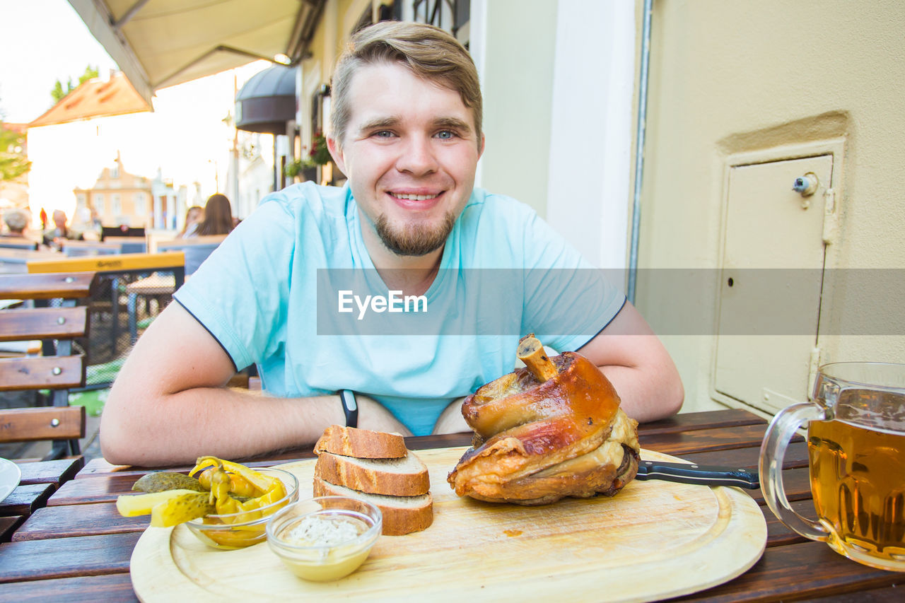 PORTRAIT OF SMILING YOUNG MAN HAVING FOOD AT TABLE
