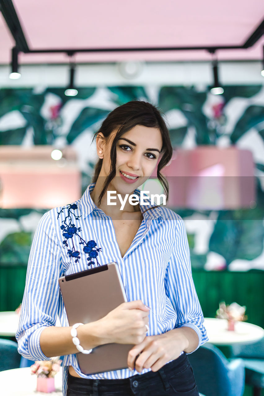 Portrait of smiling businesswoman with digital tablet standing in cafe