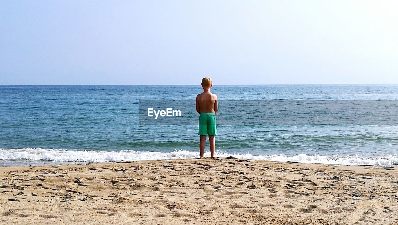 Rear view of boy standing on shore at beach