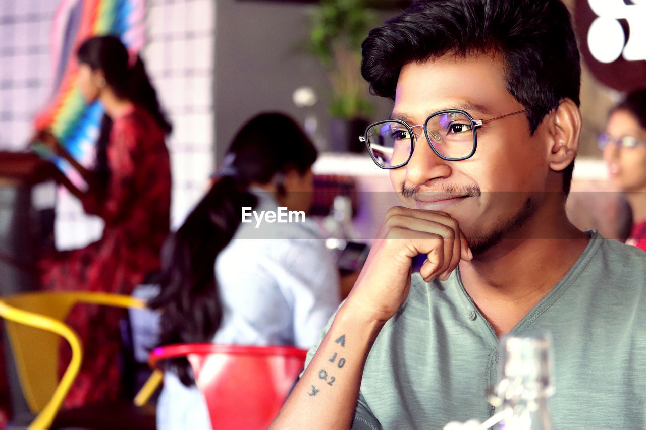 Smiling young man wearing eyeglasses looking away in restaurant