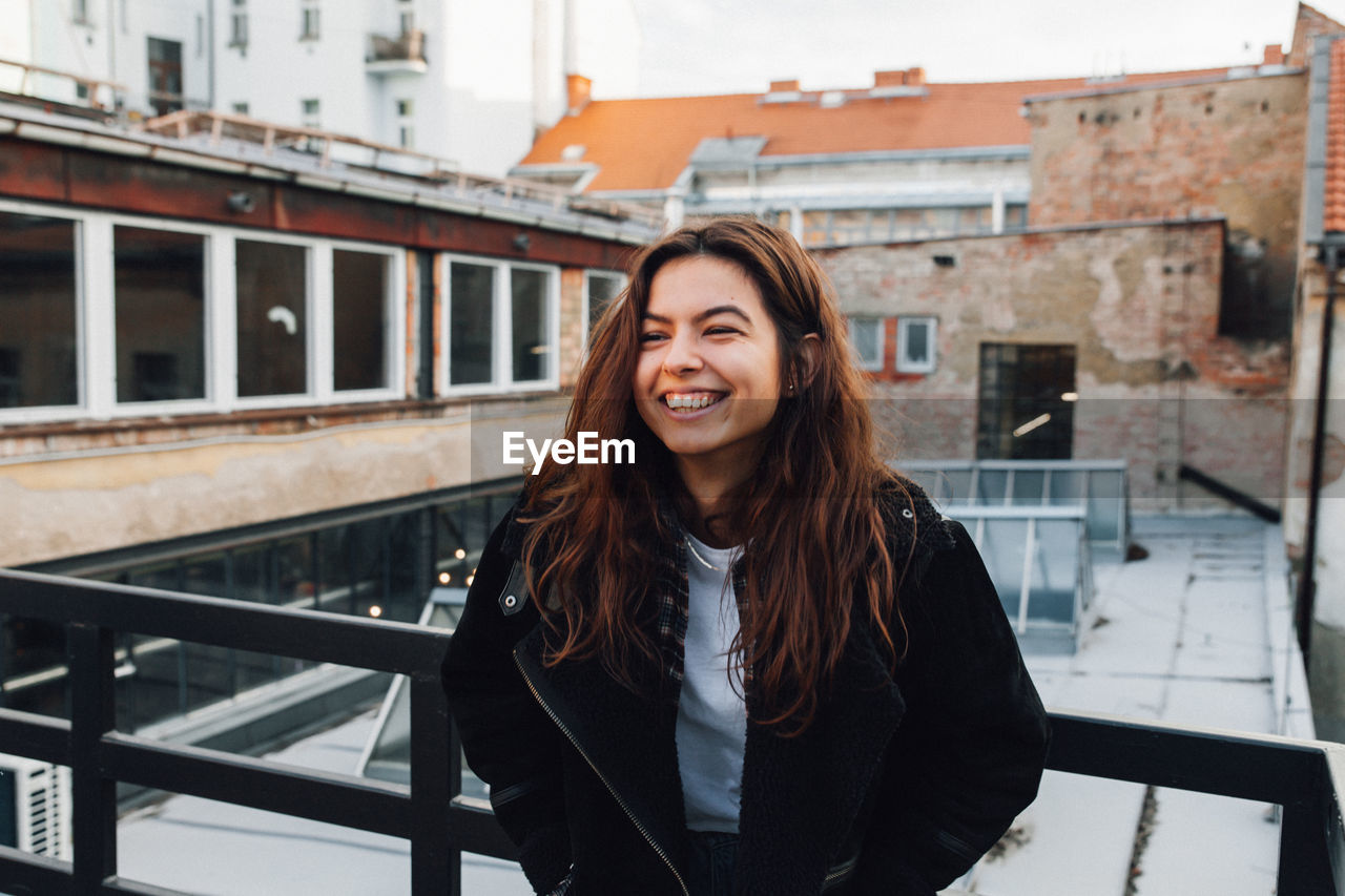 Smiling young woman looking away while standing by railing