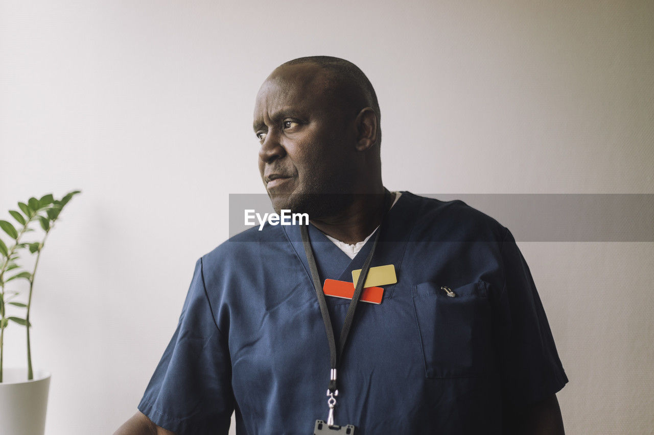 Male doctor wearing scrubs against wall at hospital